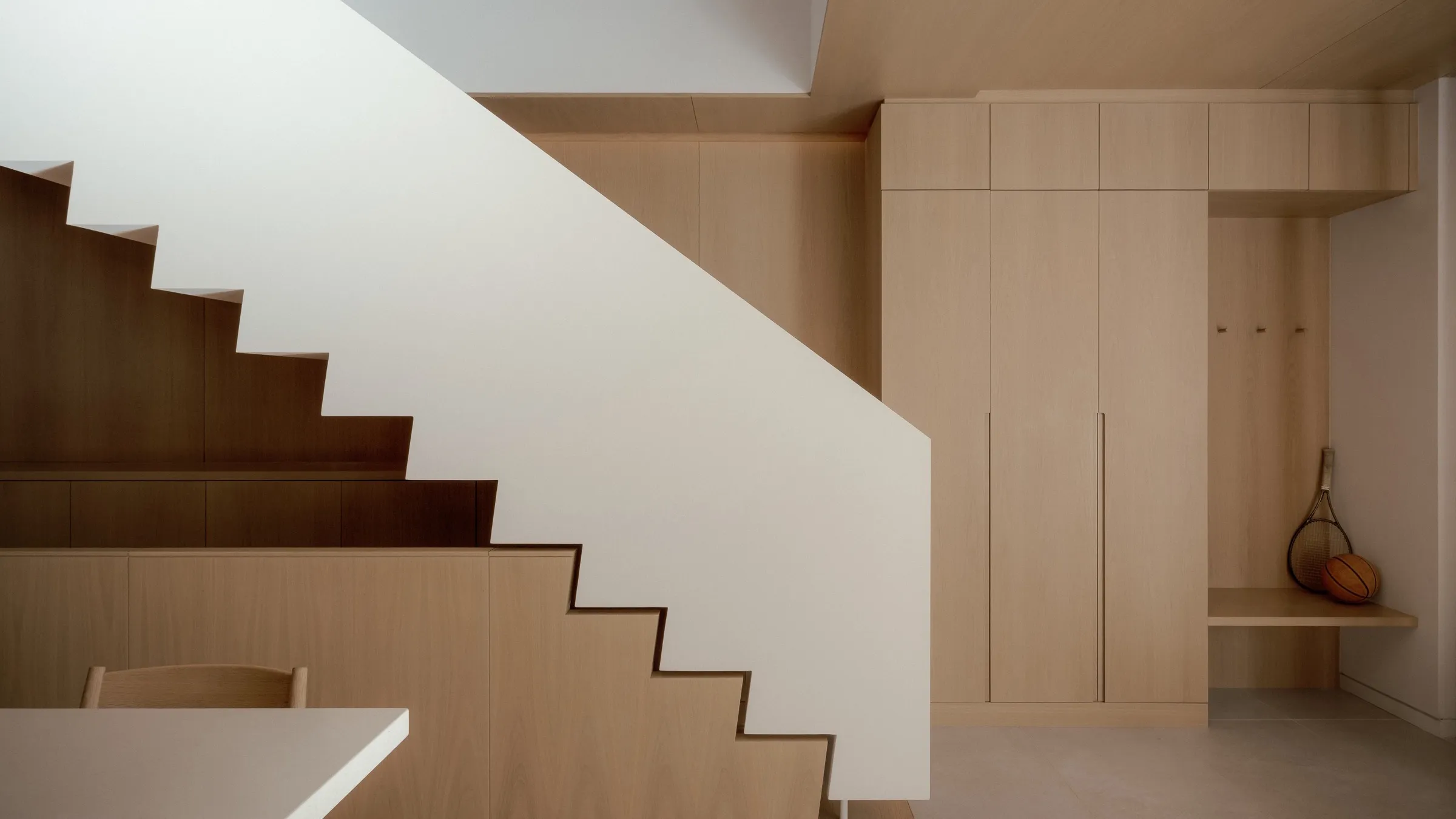 Bellwoods Residence: a white metal stair saw-toothing into a full-height white oak guard, with a mudroom bank of tall oak doors, hooks, and a cantilevered bench beyond.