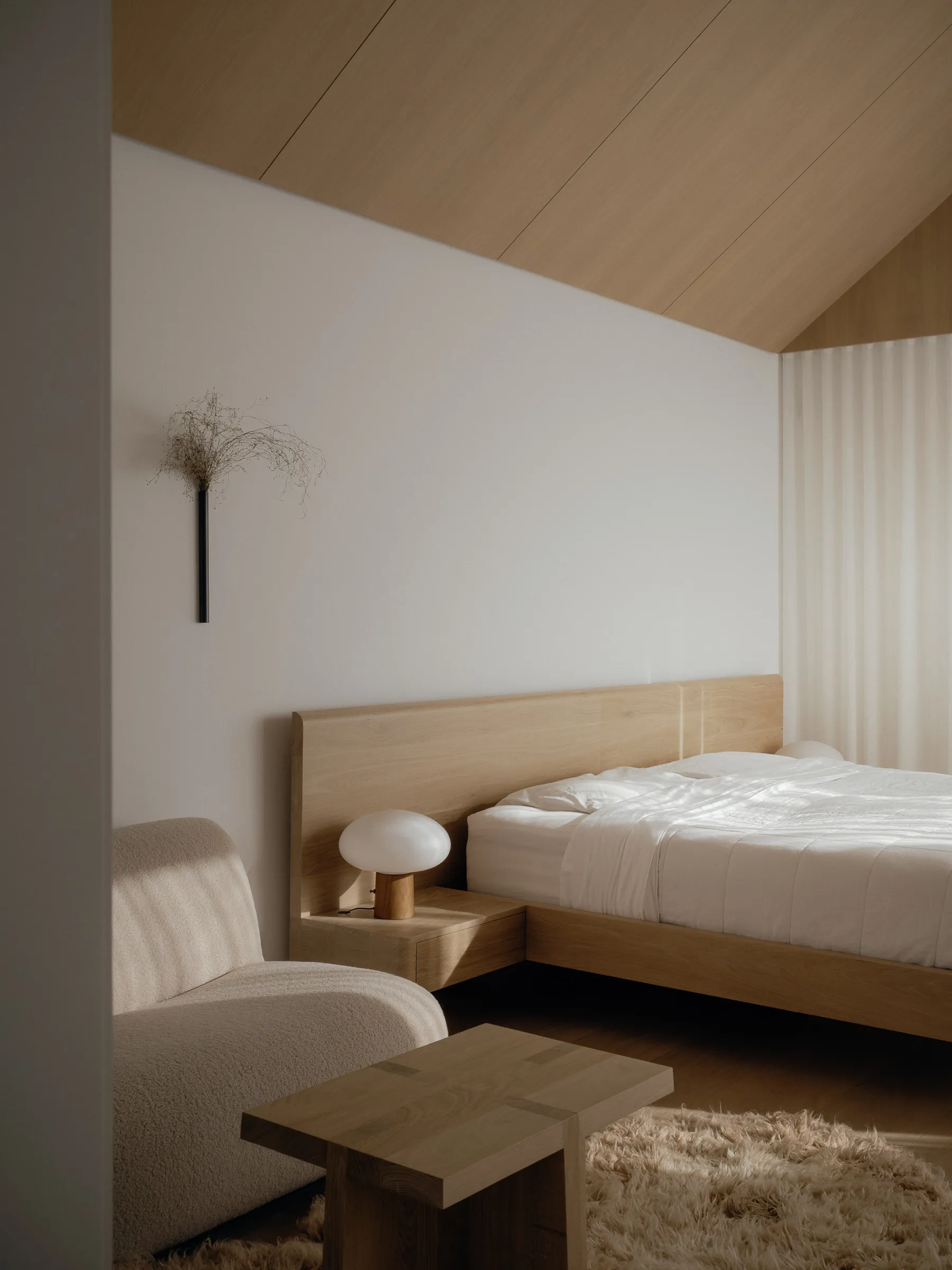 The primary bedroom at Bellwoods Residence, planked in white oak along the gable, with a full-width oak headboard and a bedside surface cantilevered off it.