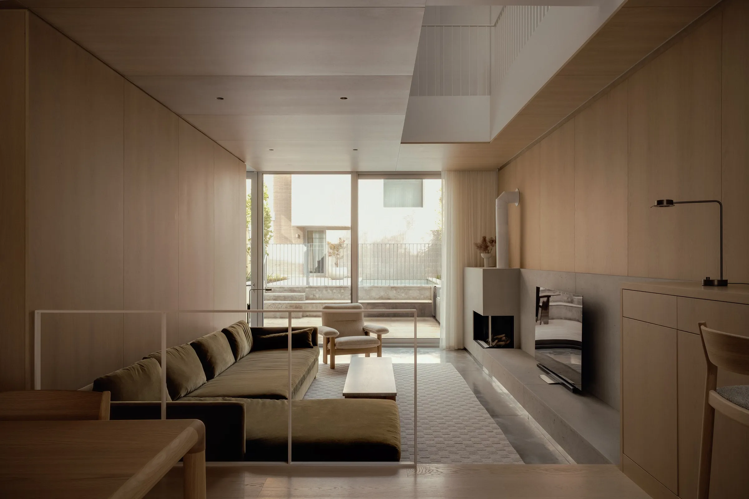 The living room at Bellwoods Residence wrapped in white oak panelling, with a plaster fireplace mass and sliding glass onto the patio.