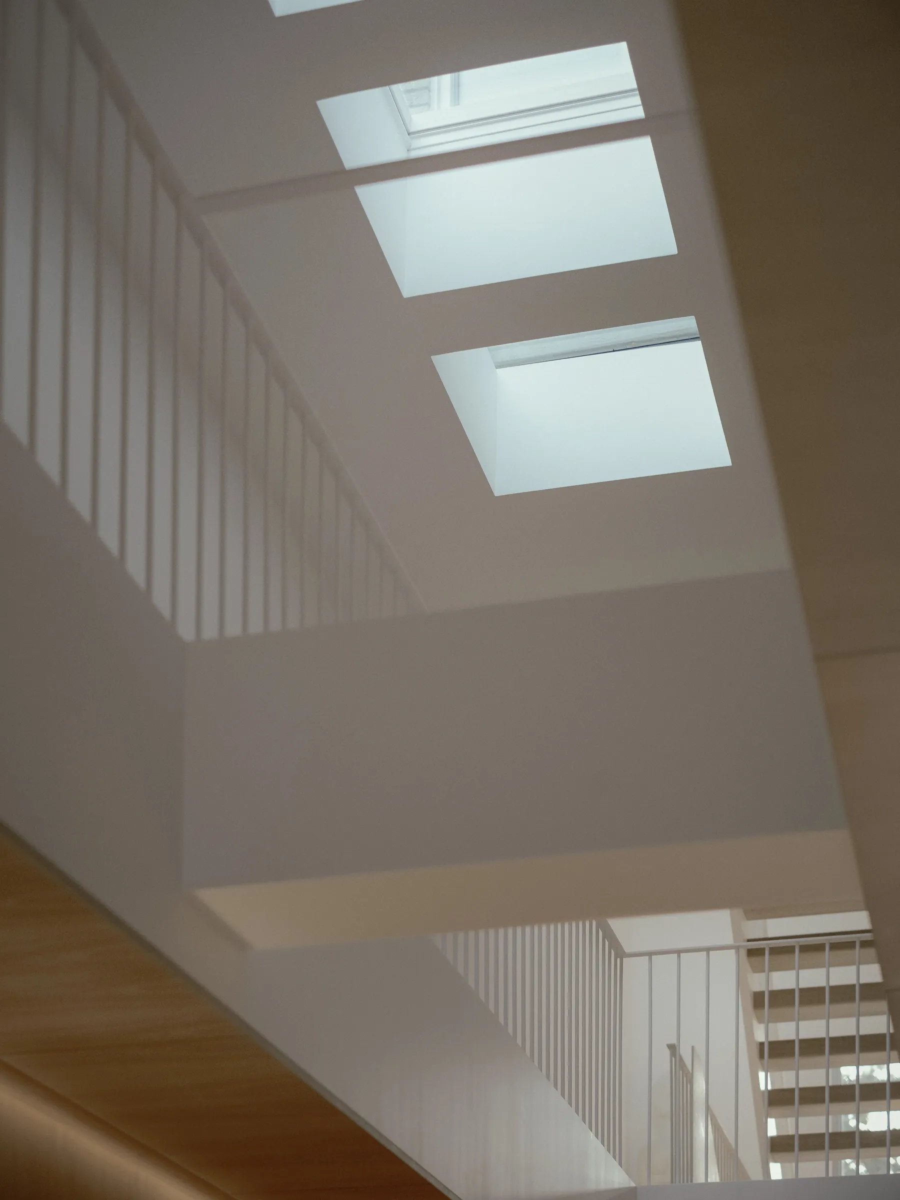 The vertical light slot at Bellwoods Residence seen from below, skylights washing the white walls with the oak edge of the void in the foreground.