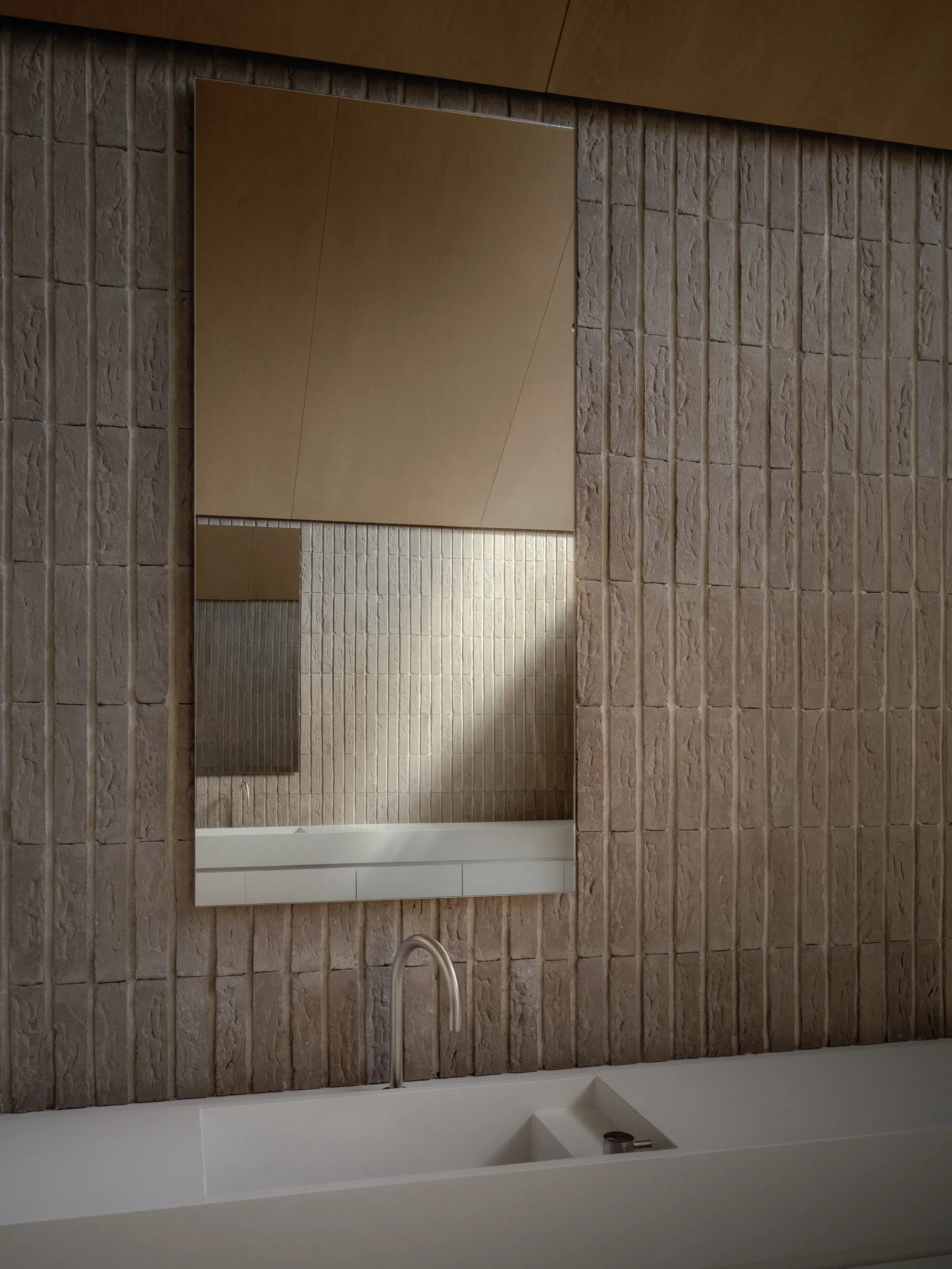 A white lacquered vanity at Bellwoods Residence with the basin formed into its top, held clear of a rough brick wall that carries the exterior material indoors.